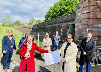 Ministerin Ina Scharrenbach überreicht Bürgermeisterin Ulrike Westkamp Förderbescheid an der Wallmauer der Zitadelle Wesel.