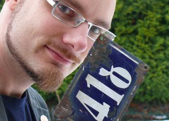 Das Foto zeigt einen Mann. Er trägt ein Schild mit einer Nummer.