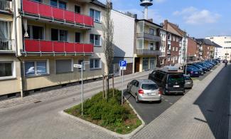 Straße mit Grünfläche, Parkplätzen und Häusern 